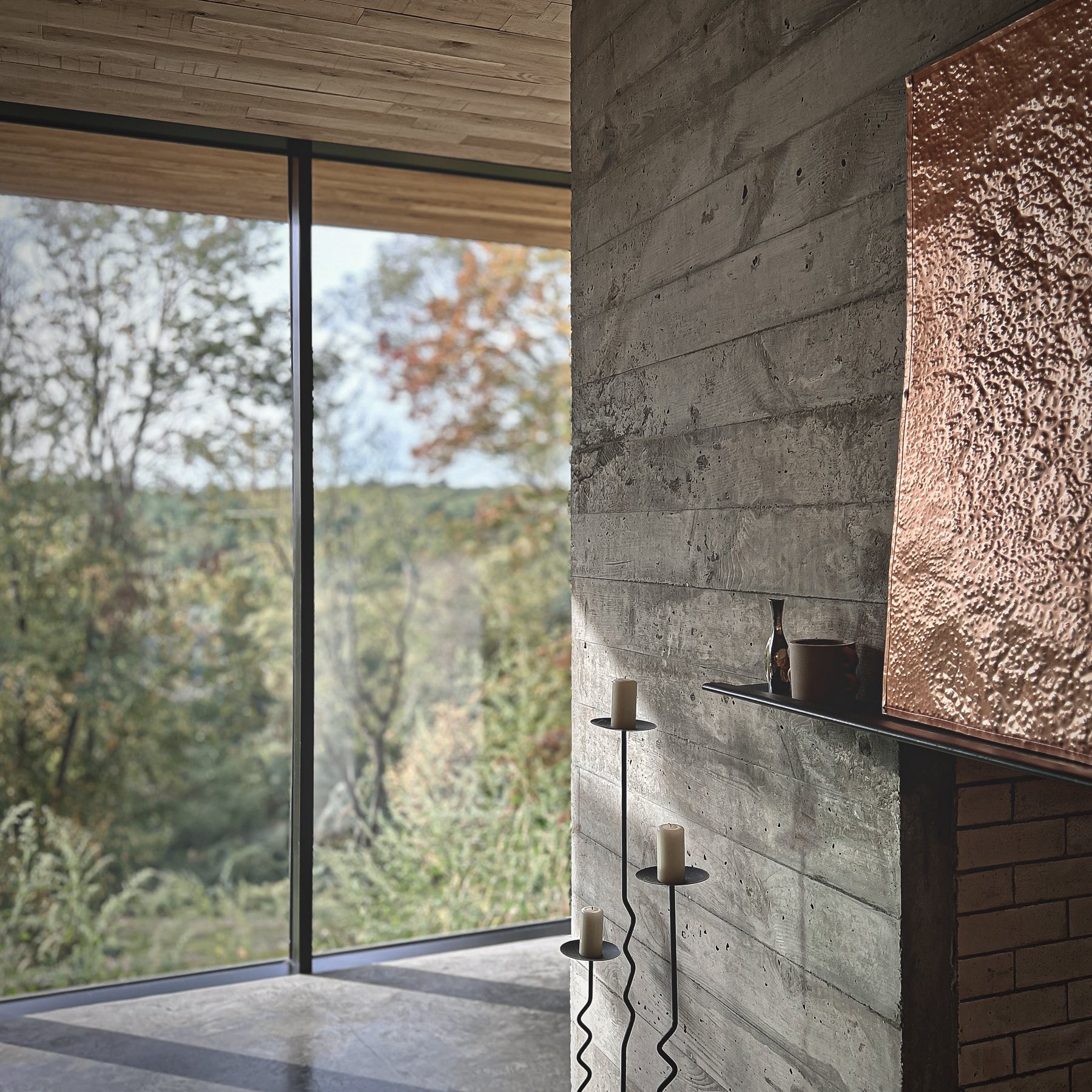 Living area with board-formed concrete wall, copper fireplace hood, and floor-to-ceiling glazing overlooking the Hudson Valley